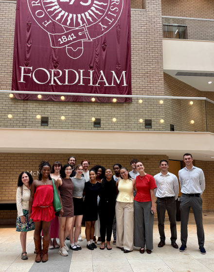 Elon University students pose for a group photo beneath a large Fordham University banner during an academic visit to New York City.